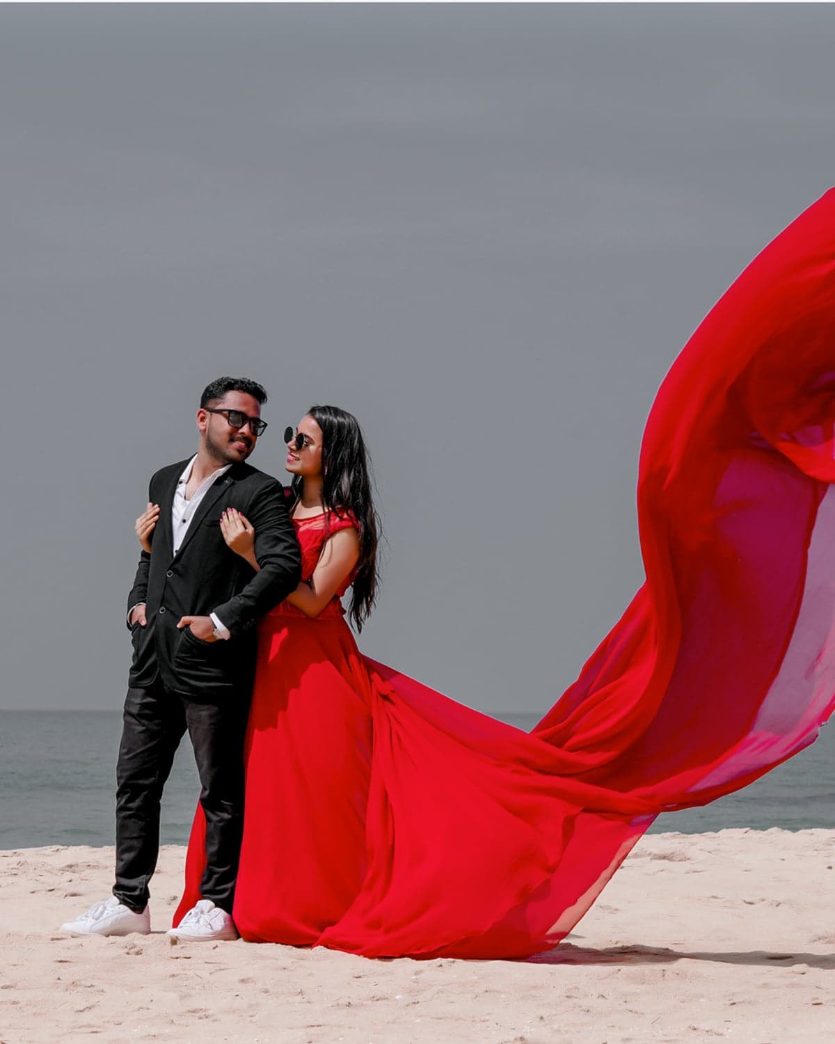 Bride and groom on the beach with a flowing red dress caught in the wind