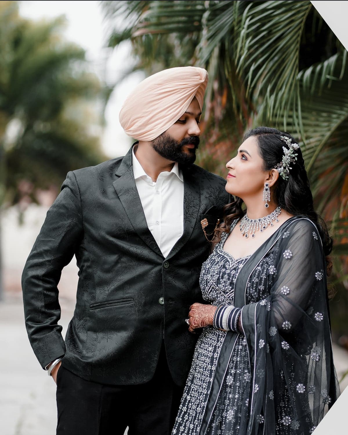 Sirish and Tejaswini in elegant black formal wear, sharing a quiet moment beneath the palms