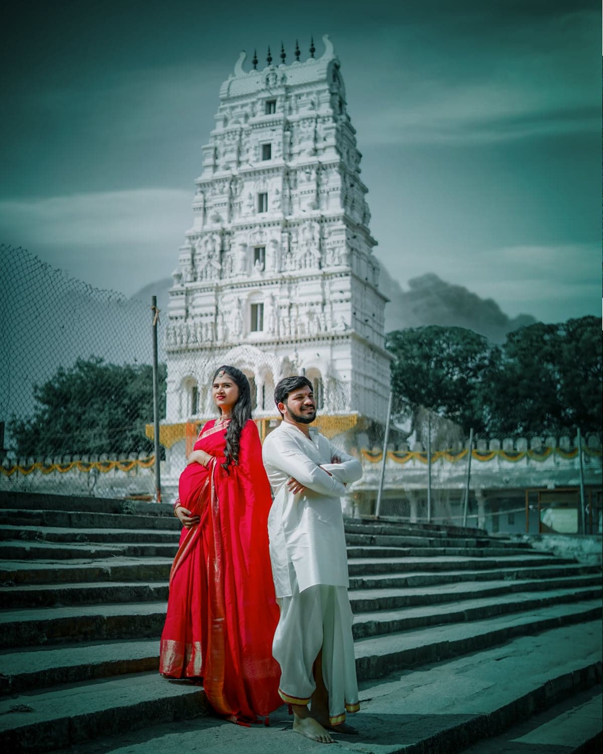 Bride and groom in a red saree and white kurta standing before a heritage temple gopuram